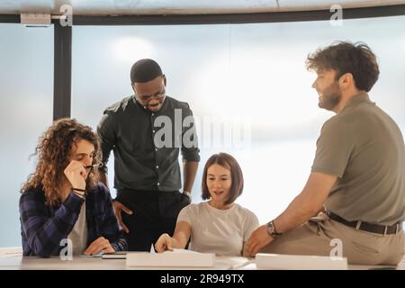 Four multiracial colleagues having fun conversation and smiling while working together at the office Stock Photo