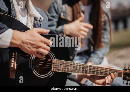 Close up of man playing guitar while sitting with his girlfriend Stock Photo