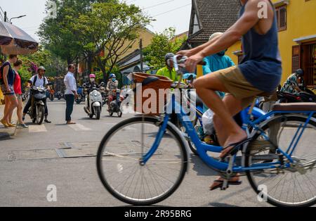 A cyclist passes in front of a lot of mopeds while pedestrians try to cross a street in the old town, Hoi An, Vietnam. Stock Photo