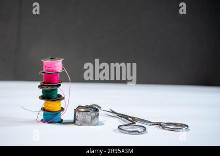 Various colored threads are wound on bobbins of a sewing machine and scissors, placed against a white background with ample copy space Stock Photo