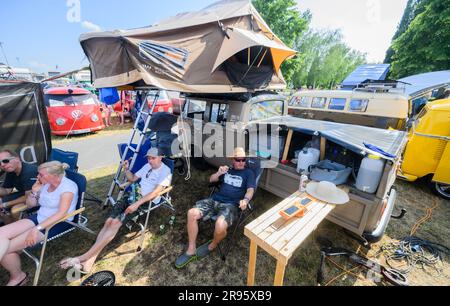 Hanover, Germany. 24th June, 2023. Festival participants sit between Volkswagen Bullis at the VW Bus Festival at the Hannover Exhibition Grounds. The festival has attracted thousands of Bulli fans to the Hanover fairgrounds since Friday. Until Sunday, different generations of the cult vehicle are shown. Credit: Julian Stratenschulte/dpa/Alamy Live News Stock Photo