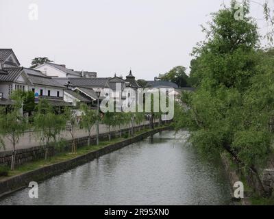 Kurashiki has a preserved canal area with the old rice warehouses painted white with black tiles, and weeping willows lining the waterside. Stock Photo