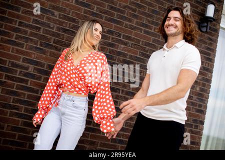 Handsome ymiling young couple in love walking in front of house brick wall Stock Photo