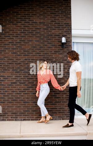 Handsome ymiling young couple in love walking in front of house brick wall Stock Photo