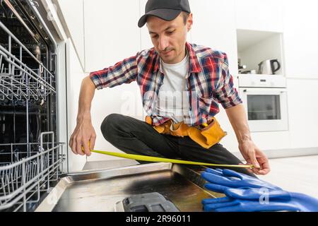 Worker using screwdriver to repair dishwasher at home stock photo Stock Photo