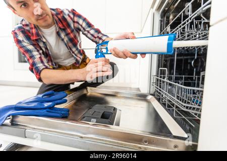 Worker using screwdriver to repair dishwasher at home stock photo Stock Photo