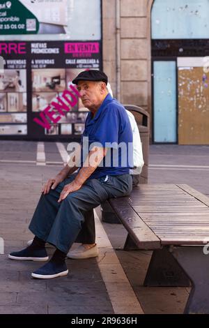 Pamplona, Spain - July, 31: An old man wearing a blue shirt sitting on a bench in the streets of Pamplona Stock Photo