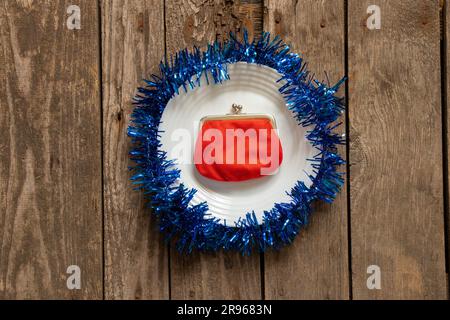 red wallet lies on a white plate decorated New Year's colored ribbon on a wooden background close-up, New Year's decor Stock Photo