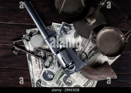 Old west Colt revolver and US banknotes and silver certificates with silver dollar coins and bronze traditional balance scale on wooden table backgrou Stock Photo