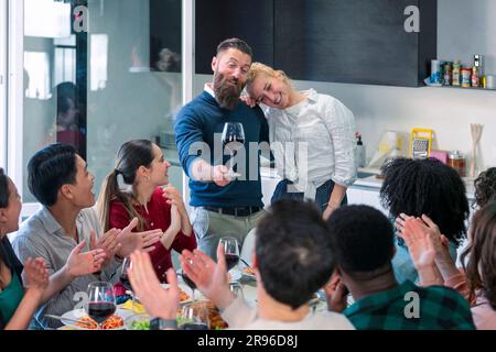 Happy young couple having fun while communicating and toasting with their friends in the dining room. friends applaud. Stock Photo