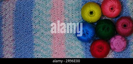 Yarn for crocheting. Several woolen multicolored balls of thread on striped pink blue crocheted background. Concept hobby of handmade needlework from Stock Photo