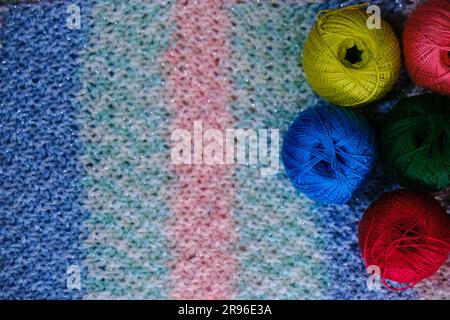 Yarn for crocheting. Several woolen multicolored balls of thread on striped pink blue crocheted background. Concept hobby of handmade needlework from Stock Photo