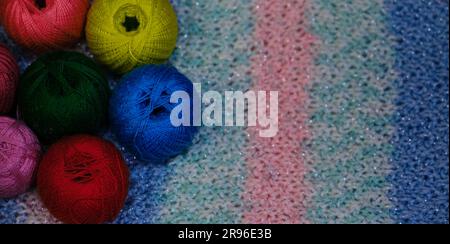Yarn for crocheting. Several woolen multicolored balls of thread on striped pink blue crocheted background. Concept hobby of handmade needlework from Stock Photo