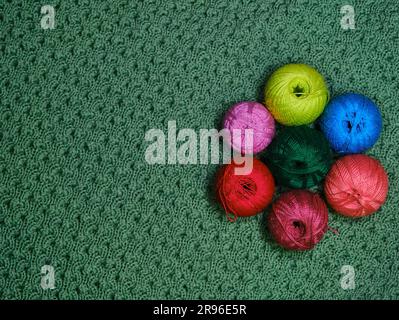 Yarn for crocheting. Several woolen multicolored balls of thread on a green crocheted background. Concept hobby of handmade needlework from home. Top Stock Photo