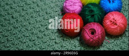Yarn for crocheting. Several woolen multicolored balls of thread on a green crocheted background. Concept hobby of handmade needlework from home. Top Stock Photo