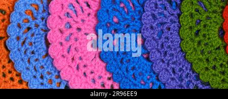 Several multicolored crocheted woolen threads decorative napkins on a green background. Close-up, slight blur and fuzziness. Top view, web banner. Stock Photo