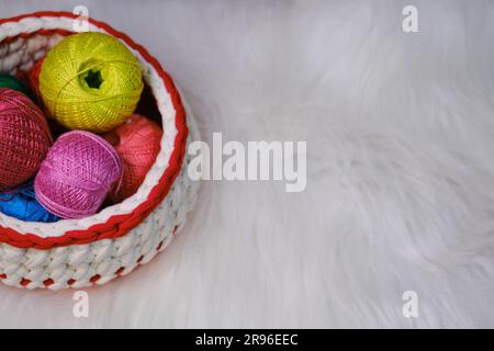 Yarn for crocheting. Several woolen multicolored balls of thread in wicker basket on white fluffy background. Top view, web banner with copy space. Co Stock Photo