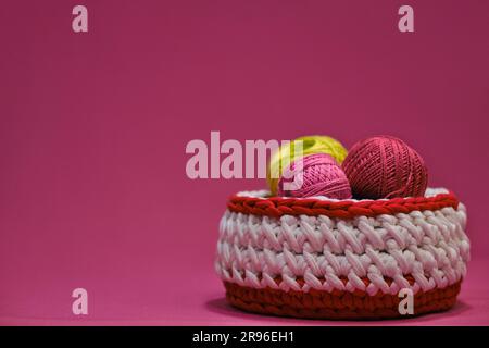 Concept craft handmade needlework hobby from home. Yarn for crocheting. Several woolen multi colored balls of thread in a wicker basket on a pink back Stock Photo