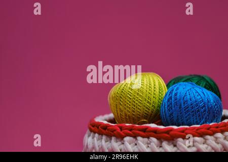 Concept craft handmade needlework hobby from home. Yarn for crocheting. Several woolen multi colored balls of thread in a wicker basket on a pink back Stock Photo