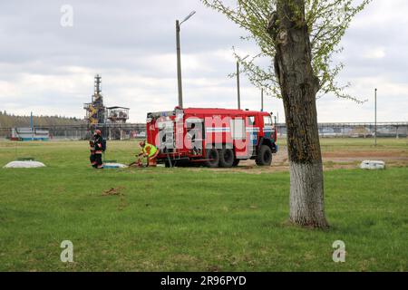 A large red fire rescue vehicle, a truck to extinguish a fire and male firefighters at a chemical, oil refinery against the background of trees. Stock Photo