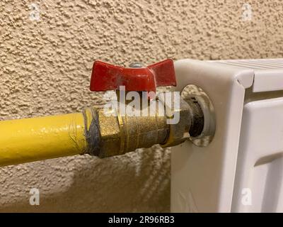 Small iron red industrial shutoff and control valves, plumbing ball valve for shutting off water and liquid flow in a metal yellow pipe. Stock Photo