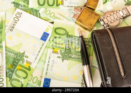 gold lighter purse clock pen on the background of green money 100 euro notes Stock Photo