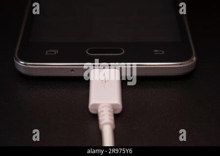 black smartphone on a black matte background with a white connected cable Stock Photo