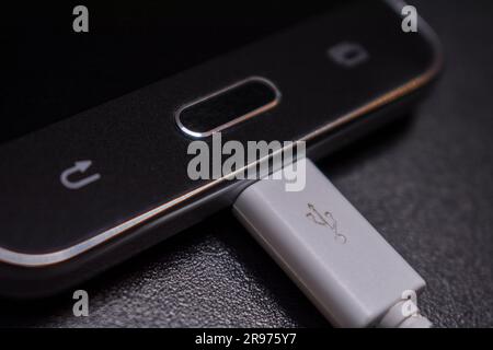 black smartphone on a black matte background with a white connected cable Stock Photo