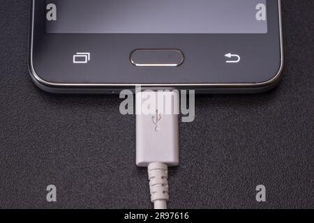 black smartphone on a black matte background with a white connected cable Stock Photo
