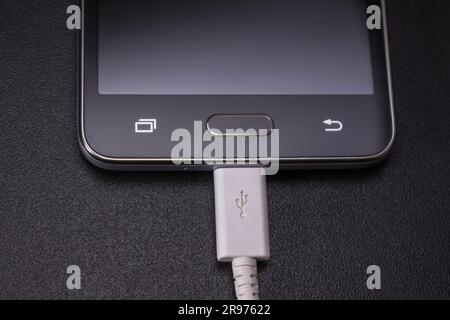 black smartphone on a black matte background with a white connected cable Stock Photo
