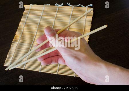 chopsticks in hand on the background of a sushi mat Stock Photo