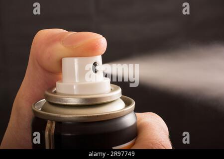 Close-up view of a human hand and pressed bottle of spray isolated on a black background Stock Photo