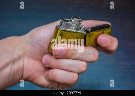 hand-held golden folding lighter on a dark background in yellow-blue tones warmth of cold Stock Photo