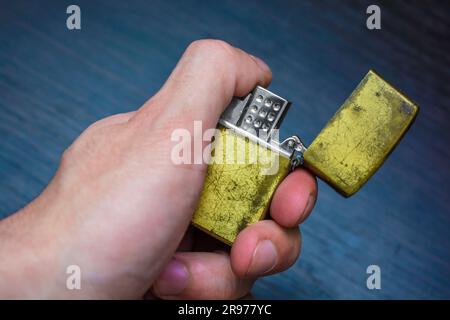 hand-held golden folding lighter on a dark background in yellow-blue tones warmth of cold Stock Photo