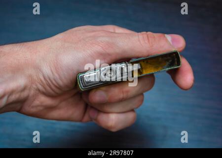hand-held golden folding lighter on a dark background in yellow-blue tones warmth of cold Stock Photo