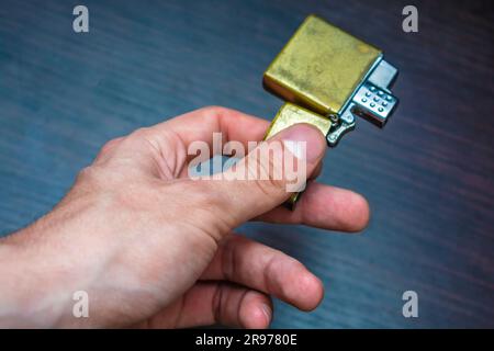 hand-held golden folding lighter on a dark background in yellow-blue tones warmth of cold Stock Photo