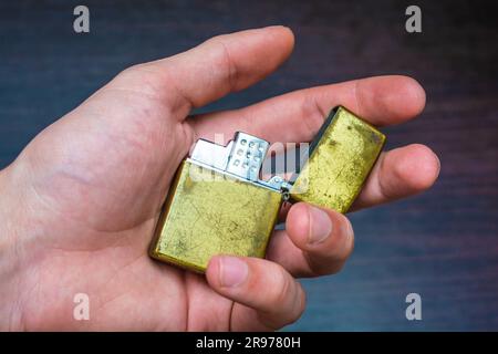 hand-held golden folding lighter on a dark background in yellow-blue tones warmth of cold Stock Photo