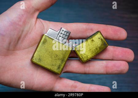 hand-held golden folding lighter on a dark background in yellow-blue tones warmth of cold Stock Photo