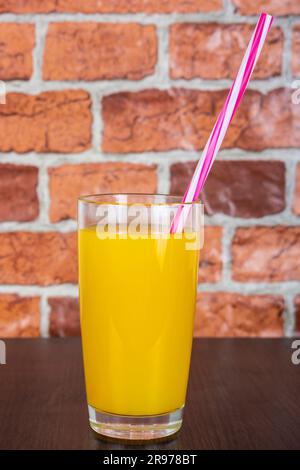 Orange juice in a glass cup with a tube on a wooden table and a background of a brick orange wall Stock Photo
