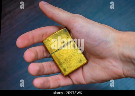hand-held golden folding lighter on a dark background in yellow-blue tones warmth of cold Stock Photo