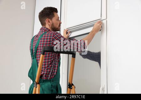 Worker in uniform installing roller window blind indoors Stock Photo