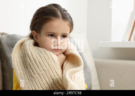 Girl with scarf around neck on sofa in room. Cold symptoms Stock Photo
