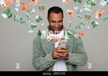 Online payment. Man buying something using mobile phone on light grey background. Euro banknotes flying out of gadget demonstrating process of money t Stock Photo