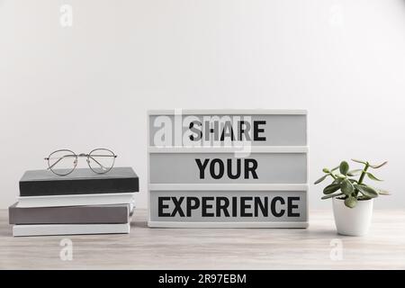 Motivational phrase. Letter board with text Share Your Experience, books, glasses and houseplant on wooden table Stock Photo