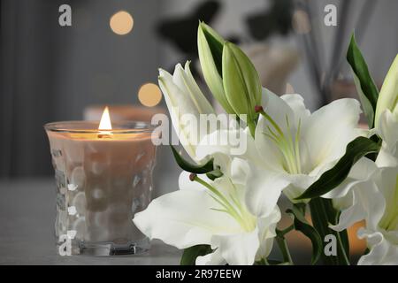 Funeral. White lilies and burning candle indoors, bokeh effect Stock Photo