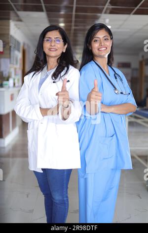 Full length profile shot of an Indian female doctor standing back to back. Senior doctor in a white suit and nurse in blue uniform. Stock Photo