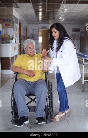Indian Nurse looking very happy greeting a senior patient in a wheelchair at the hospital and smiling - healthcare concepts. Stock Photo