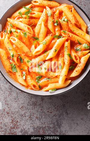 Penne pasta in creamy tomato or pink sauce closeup on the bowl on the table. Vertical top view from above Stock Photo