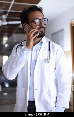 Medical professional portrait in hallway of hospital dressed in scrubs and lab coats, with stethoscopes. Indian decent talking on a mobile phone. Stock Photo