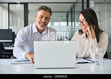 2 diverse team coworkers working together looking at laptop discussing project. Stock Photo